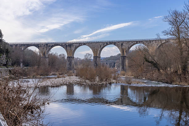 Stone arched viaduct reflecting in the tranquil waters of the Ardeche river in France