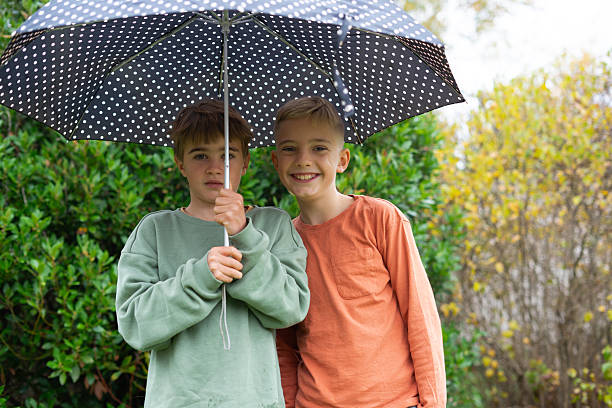 istock Two smiling boys holding umbrella together under rain 2251825842
