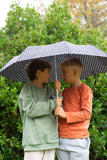 istock Two young boys sharing umbrella on a rainy day 2251825845