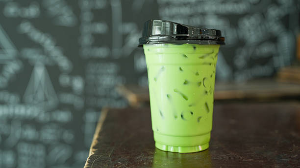 Refreshing green iced beverage in clear cup with black lid, featuring ice cubes. drink is vibrant and appealing, perfect for warm day
