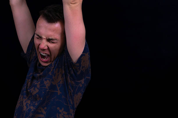Energetic Studio Shot Of A Young Man Cheering With Arms Raised And Shouting, Wearing A Navy Patterned Tshirt Against A Black Background, Perfect For Success, Winning, Goals, And Celebration Themes.