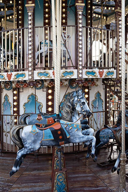 Ornate dapple grey horses on a vintage two-story carousel. Illuminated with warm lights, this classic fairground ride evokes a magical sense of nostalgia and wonder.