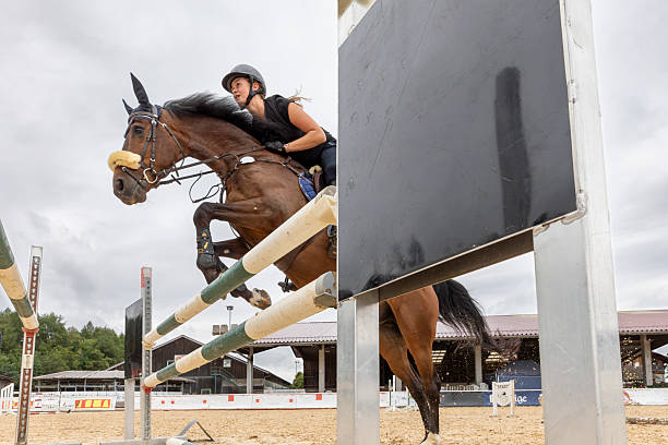 Male equestrian athlete jumping a white sport horse over a red and yellow barrier in a sand arena. Intense show jumping action demonstrating agility and speed. Antalya - Turkey