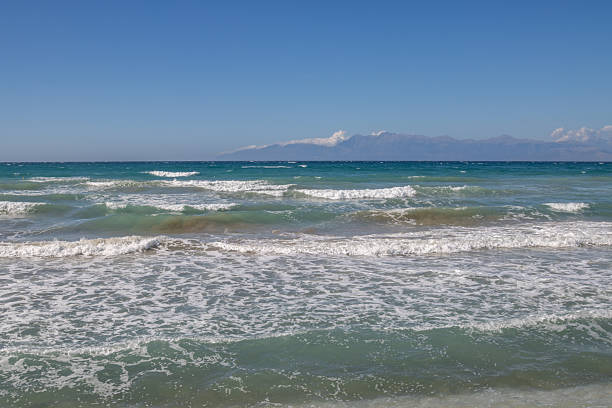 Ionian sea with dramatic waves during a late summer day. Albanian mountains in the background. Blue sky with white clouds. North of the island Corfu (Korfu), Acharavi, Greece.