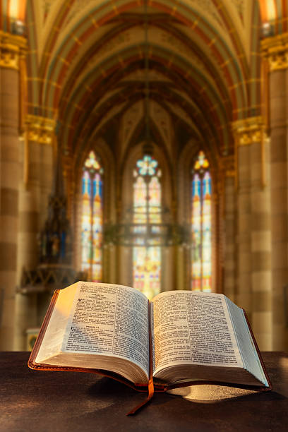 istock Open Bible in sunlight near stained glass window 2251845045