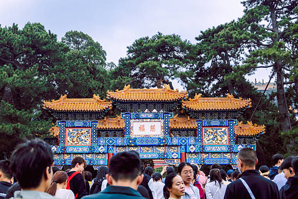 Beijing, China - October 5, 2025: Richly decorated traditional gate in Summer Palace with colorful painted panels golden roof tiles and crowd of visitors at historic palace complex