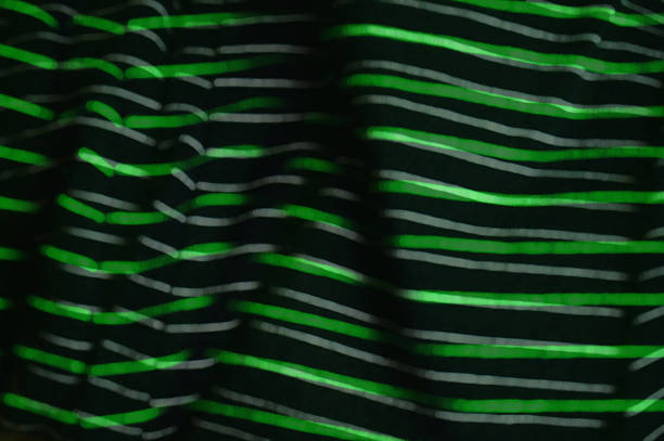 A dark fabric background features bright green neon, wavy stripes forming a bold, energetic pattern. Abstract, modern design suitable for fashion, interior, or technology-themed visuals and branding.