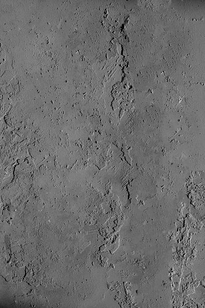 A close-up view of a rough, uneven gray surface resembling concrete or plaster. The texture features ridges, indentations, and weathered patches, offering a raw and tactile aesthetic. Ideal for use in architectural backgrounds, design mockups, material studies, or abstract compositions that emphasize industrial minimalism and surface detail.