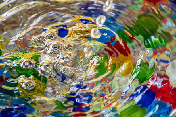 Clear water splashing and creating ripples over a vibrant background of colorful glass beads.