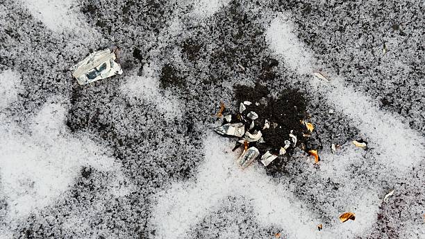 This photo shows fragments of a broken ceramic object scattered across snow. The white shards with blue ornamentation and orange details lie on partially melted snow, revealing dark soil or pavement underneath. The contrast between the cold environment and delicate ceramic creates an emotional effect, symbolizing loss, fragility, transformation, or remnants of the past. The image is ideal for use in social campaigns, blogs, visual storytelling, artistic projects, articles on ecology, urban life, memory, and as a background or thematic element for creative mockups.