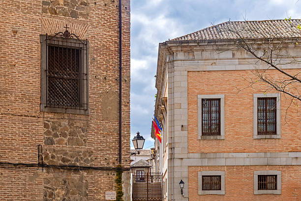 Close-up of two contrasting Toledo buildings: one rustic brick with a gridded window, the other smoother with stone quoins and a tiled roof, framing a street view