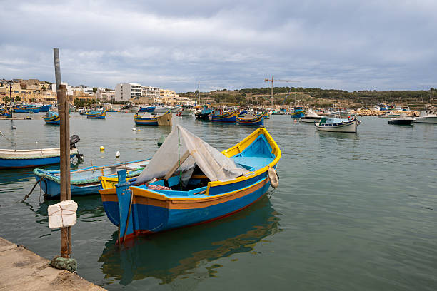 Colorful Maltese fishing boats, called Luzzus, bob gently in the harbor. They are docked, awaiting their next voyage to catch fish in the Mediterranean Sea.