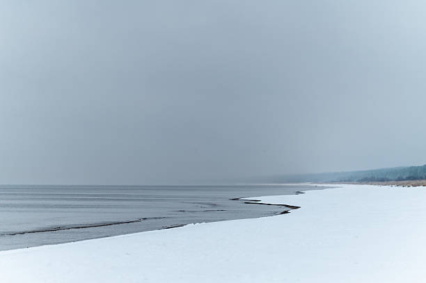 Minimalist winter seascape showing frozen Baltic Sea with natural ice formations creating winding patterns along snowy beach.