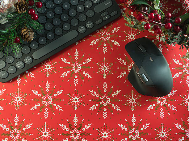 Christmas Tech Desk Setup - Overhead view of a black computer keyboard and mouse on a festive red background with snowflake patterns, adorned with Christmas garland. Perfect for holiday work themes.