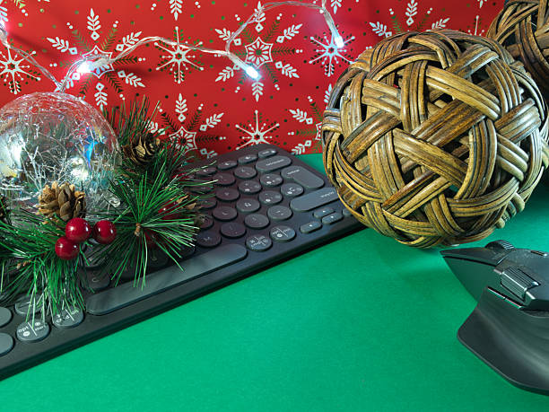 istock Festive Tech Decor - Holiday-decorated office desk with keyboard, mouse, ornaments, and string lights on a green surface against a red snowflake background. 2251876719