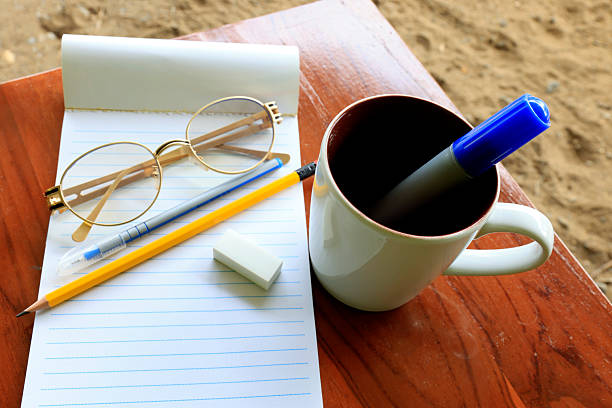 Workspace with notebook, pencil, pen, eyeglasses, coffee mug, and stationery on wooden table. Concept of work, study, education, creativity, and daily lifestyle