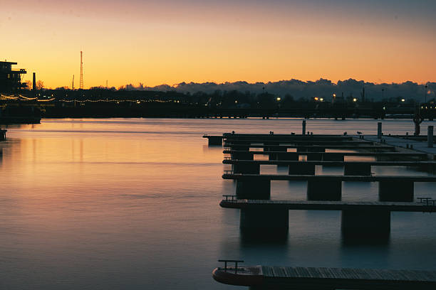 Tranquil evening scene at Noblessner Port in Tallinn, Estonia. Silhouetted piers stretch into calm water under a vibrant orange and purple sunset sky, creating a serene maritime atmosphere.
