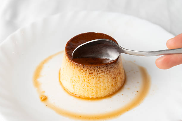 A woman sits at a cafe table, using a spoon to eat a dessert from a glass dish.
