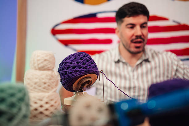 Man winding purple yarn into a neat ball with a ball winder, focused on a cozy, creative home crafting project in studio