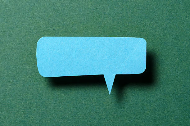 Blue blank cut out paper speech bubble with shadow and copy space for text on green background, close-up flat lay top view backdrop
