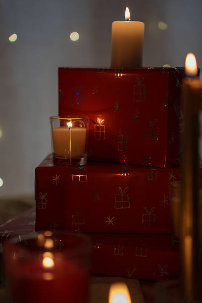 istock warm festive scene with glowing candles on stacked red gift boxes adorned with shiny patterns, creating a cozy holiday atmosphere against a soft blurred light background, joyful, vibrant, twinkle 2251902361