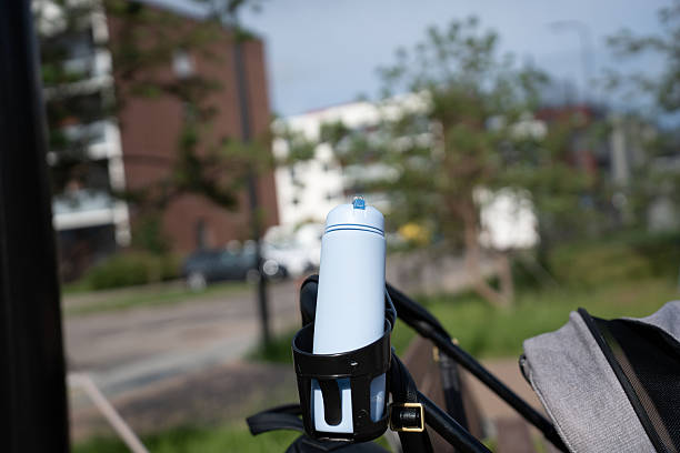 istock a pastel blue thermos bottle securely nestled in a black holder attached to a stroller, set against blurred urban buildings and greenery on a sunny day, creating an outdoor context, shade, design 2251902624