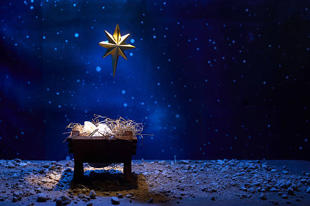 A glowing star over a manger with a stone backdrop and blue night sky.
