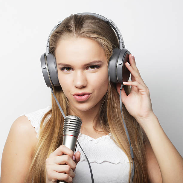Beautiful young woman with microphone and headphones on gray background