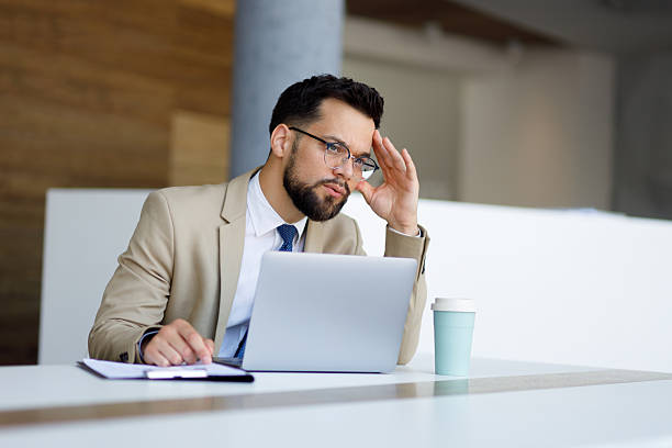 istock Businessman thinking with hand on head at office desk, experiencing stress and problems while working on laptop 2251910212