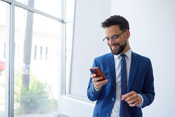 istock Businessman smiling, reading messages on mobile phone, using corporate technology at modern office window 2251910693
