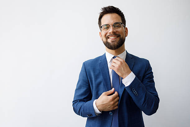 istock Confident businessman fixing tie, smiling on a white background, representing success and professionalism 2251912353