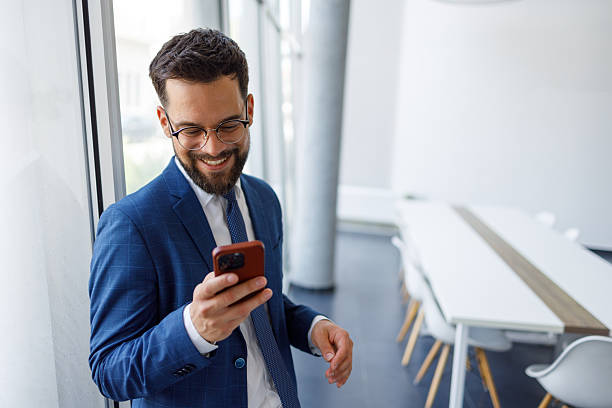 istock Smiling young businessman using smartphone in modern office, leaning on window and checking mobile content 2251912943