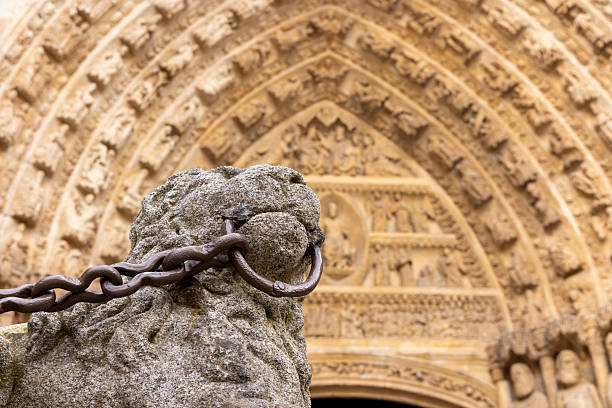 A stone statue with a chain around its neck is in front of a building. The chain is rusty and the statue appears to be chained to a stone pillar. The building is old