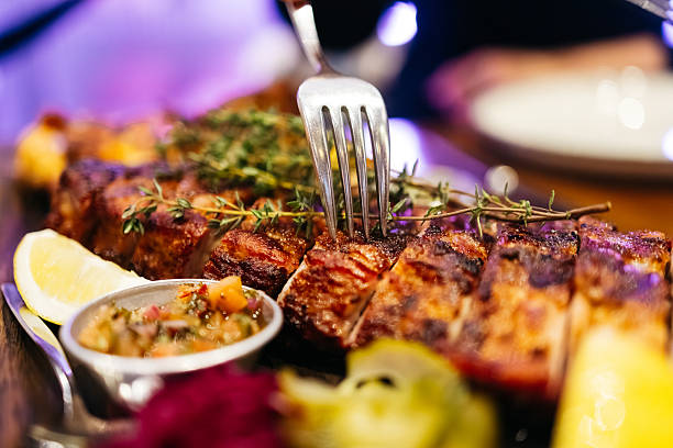 Grilled meat dish garnished with fresh herbs, lemon slices, and colorful sauces on a wooden platter, showcasing culinary artistry and vibrant presentation