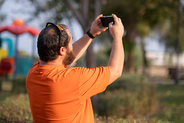 Man performing daily activities in public park. Everyday life scene of man in city park. Casual man reading, talking, eating and checking time outdoors.