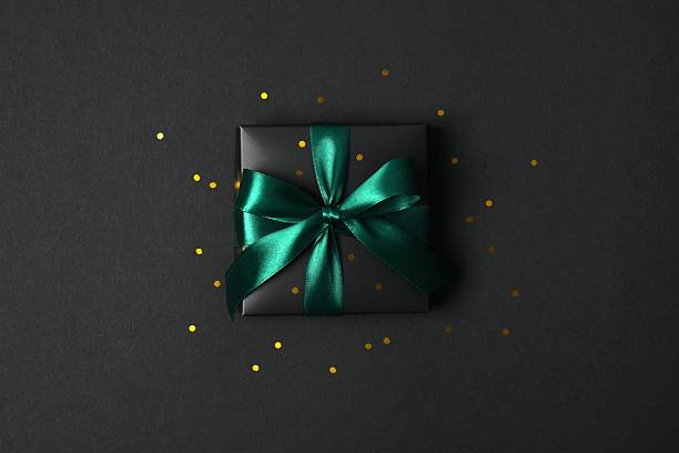 istock Beautiful black gift box tied with green bow on black background 2251920233