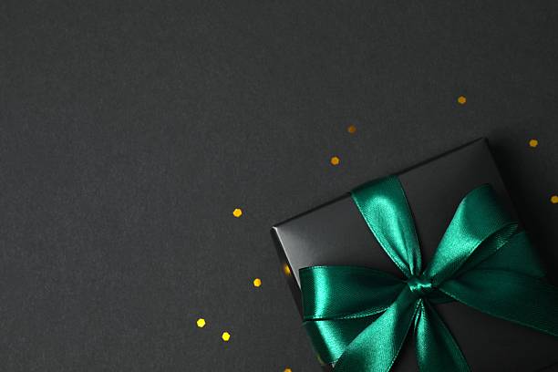 istock Beautiful black gift box tied with green bow on black background 2251920235