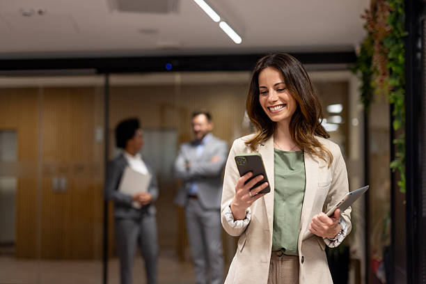 istock Smiling businesswoman using smartphone in modern office corridor 2251921378