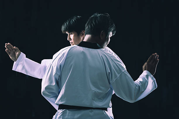 Martial arts fighters stand back to back practicing defensive blocks with focused posture strength and balanced motion in dark studio lighting