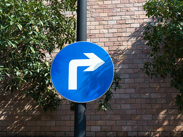 istock Blue right-turn sign by brick wall and leafy trees. 2251928537