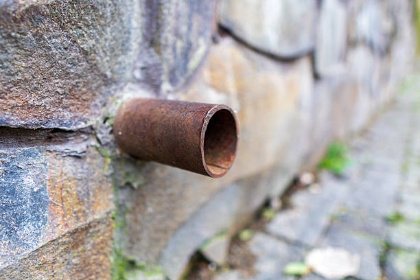 A rusty pipe is sticking out of a wall. The pipe is bent and has a hole in it