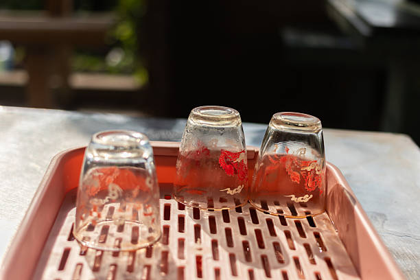 Still life shot of three small glass cups, traditionally used for street iced tea (trà đá) in Vietnam, with red residue, drying on a plastic tray outdoors