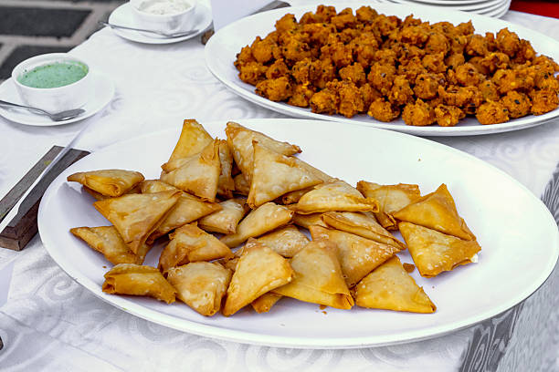 A close-up view of a party spread featuring crispy triangular samosas and savory pakora fritters alongside small bowls of green and white dips
