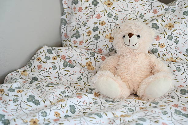 istock White, soft teddy bear in a child's bed with floral pattern bedsheets 2251937152