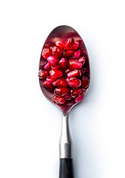 Red pomegranate seeds on a spoon, top view. Isolated on white background, studio shot.