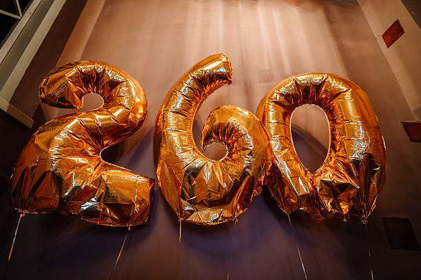 Large golden balloons shaped as numbers 2, 6, and 0 are displayed against a softly lit background, celebrating a special occasion with vibrant colors and festive atmosphere