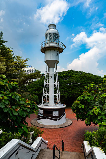A tall white lighthouse at Fort Canning standing against a dramatic sky, framed by lush trees, showcasing heritage architecture and outdoor scenery.