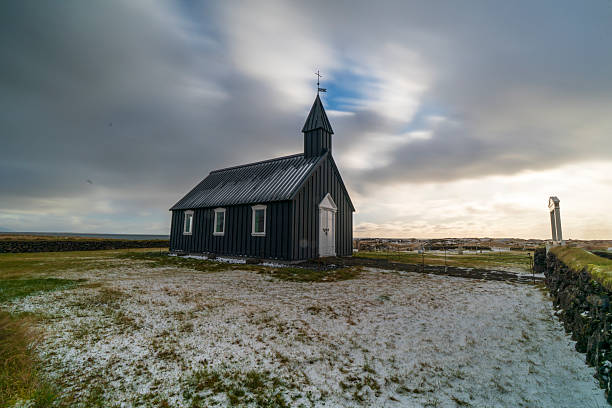 views of Búðir’s iconic black church set against a vast Icelandic landscape. Surrounded by open fields, distant mountains, and shifting light, the stark contrast highlights the solitude and timeless beauty of this remote place.