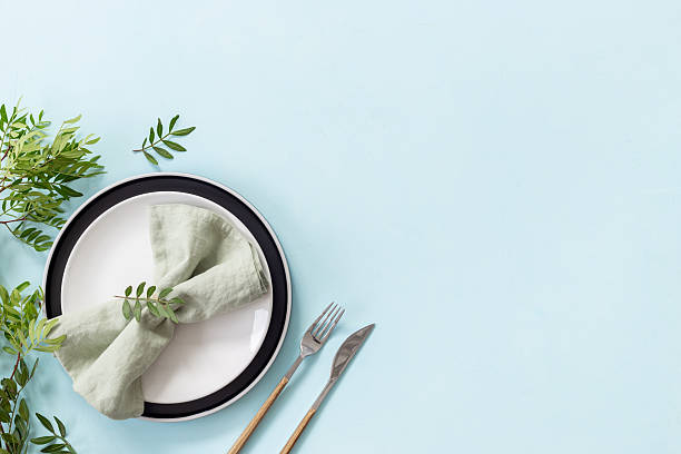 istock Beautiful minimalistic table setting with empty plate and napkin - green leaves decorated on blue background, flat lay. Top view 2251958984