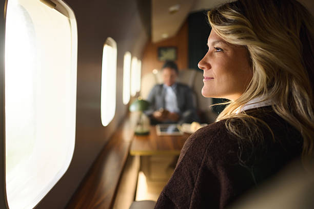 Profile view of smiling female passenger day dreaming through window while traveling by private jet.